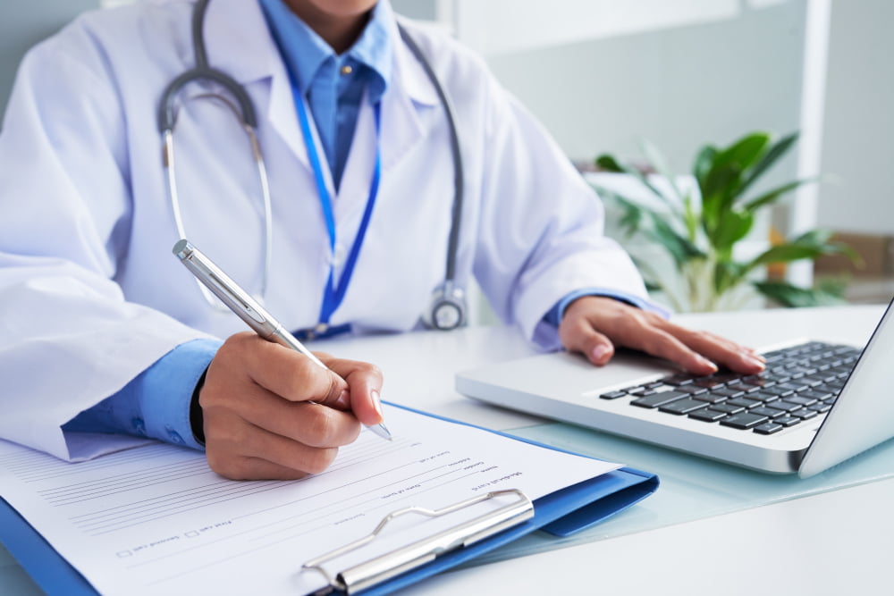 Qual a causa e diagnóstico da gastrite? 4 hands unrecognizable female doctor writing form typing laptop keyboard 3
